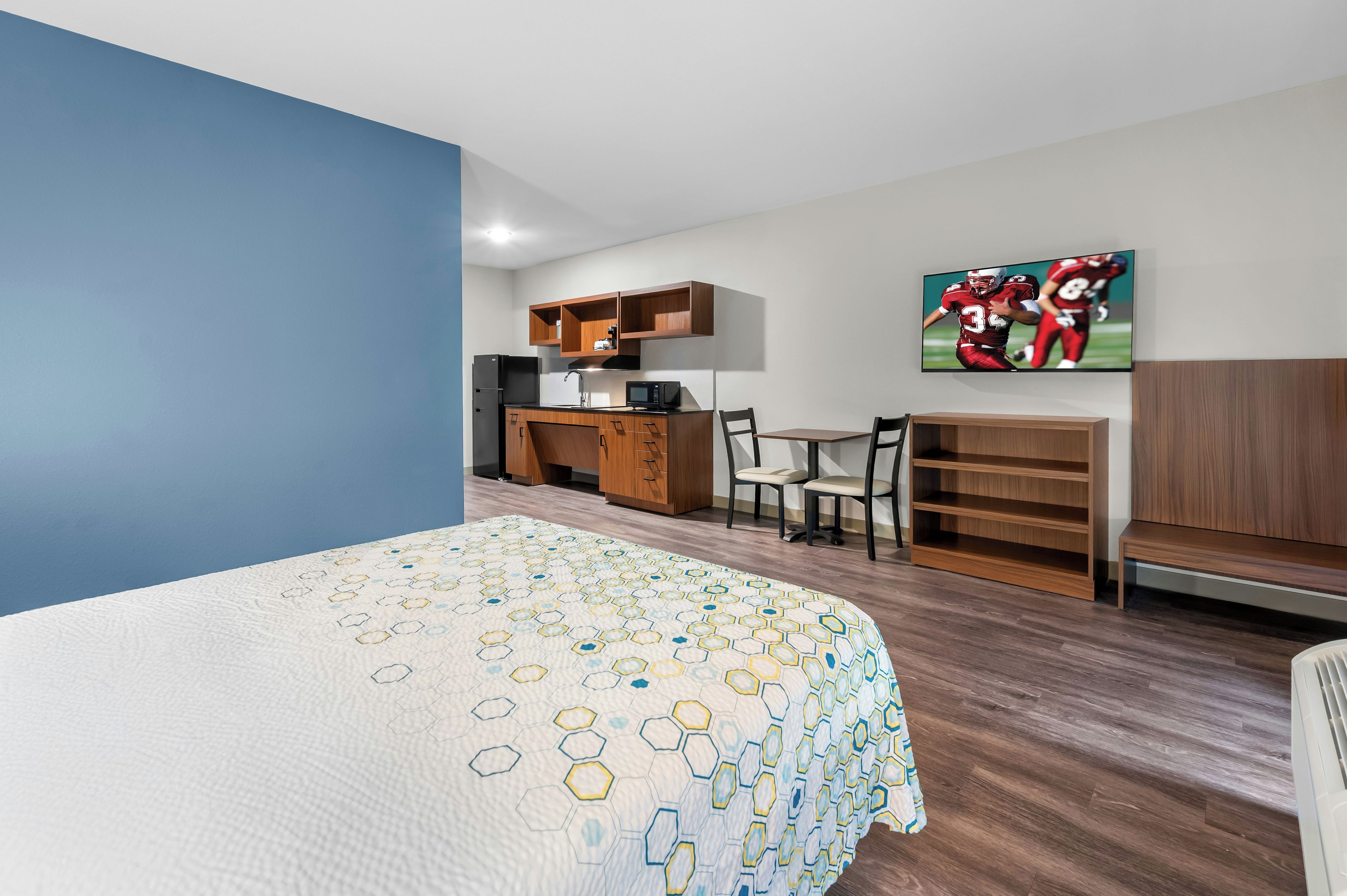 A hotel room with a bed, a desk, a chair, a microwave, and a TV.