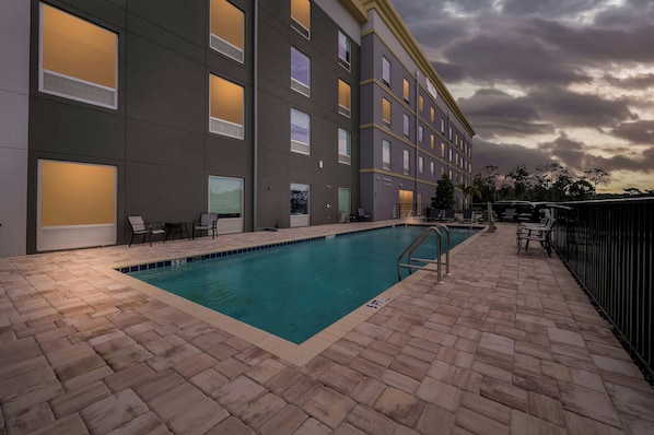 A swimming pool with a tiled deck, a building with multiple windows, and a cloudy sky.