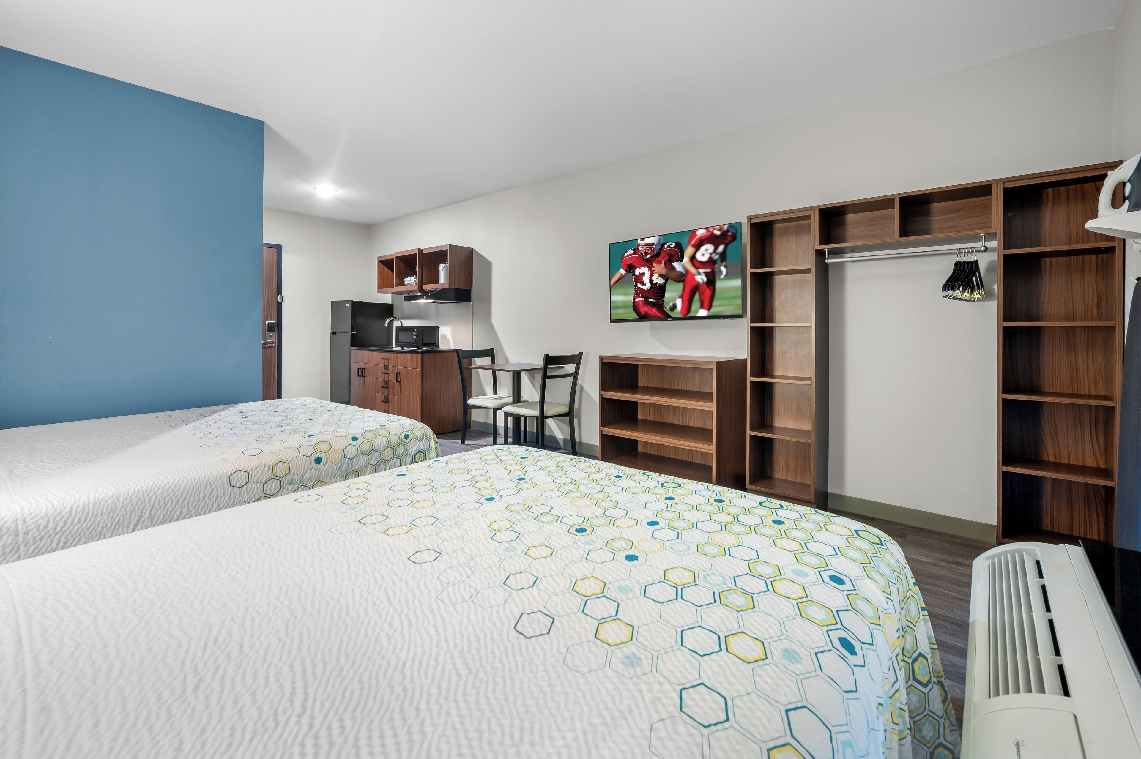 A hotel room with two beds, a desk, a chair, a TV, and a wardrobe.
