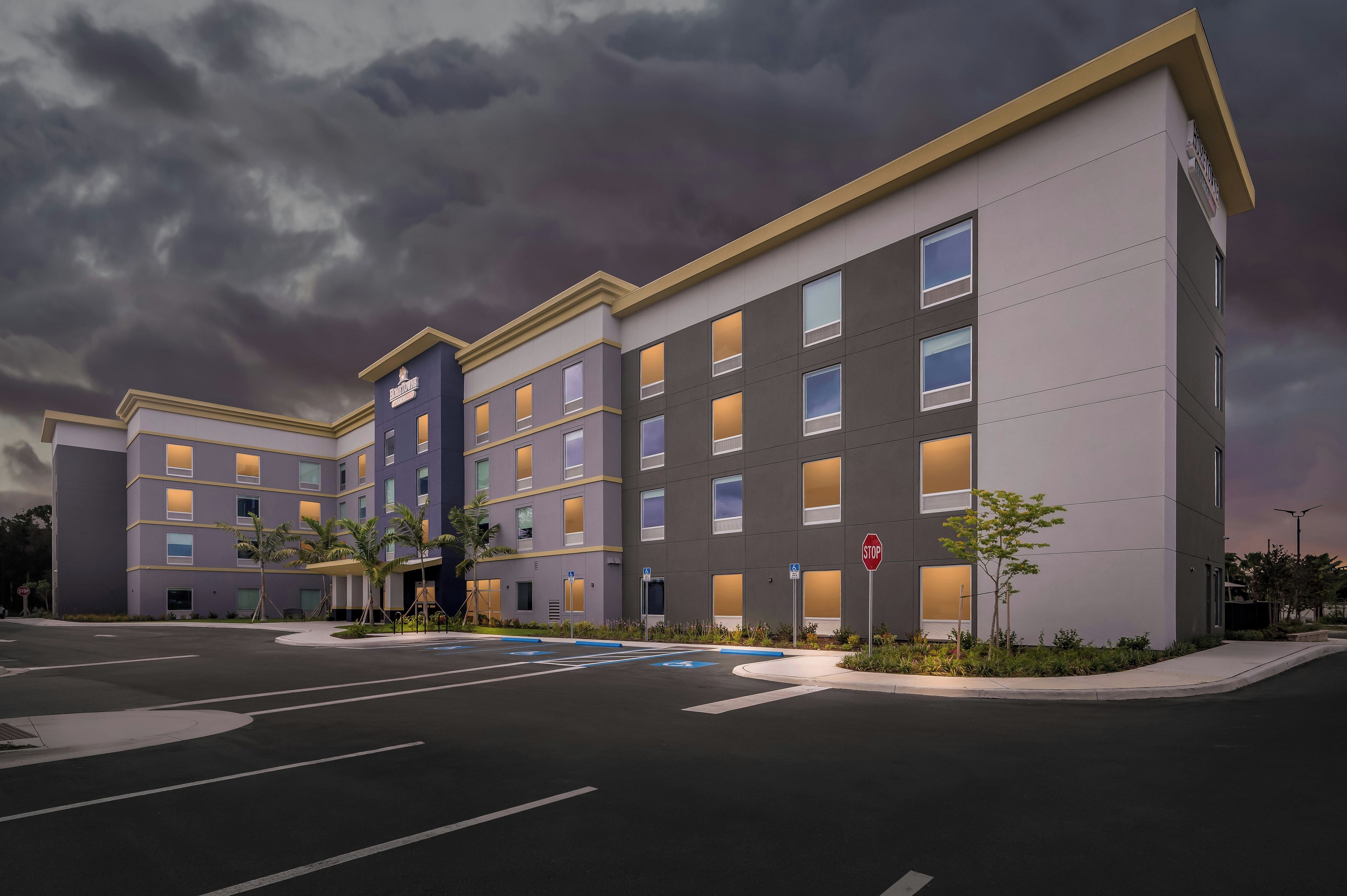 A multi-story hotel with a modern design, featuring a prominent entrance, a parking lot, and a stop sign.