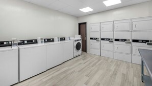 A laundry facility with multiple washing machines and dryers, a wooden floor, and a door. - HomeTowne Studios by Red Roof Fort Myers (Fort Myers)