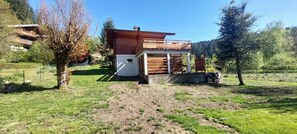 Una casa de fusta de dos pisos amb un balcó, envoltada d'una zona verda i arbres.