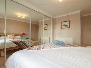 A hotel room with a large mirror, a bed with white linens, a blue towel, and a patterned throw. - Honeysuckle Rise (Looe)