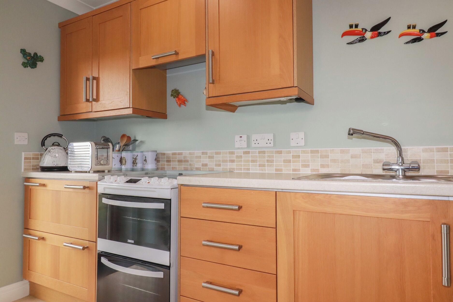 A kitchen with wooden cabinets, a built-in oven, a toaster, and a sink.