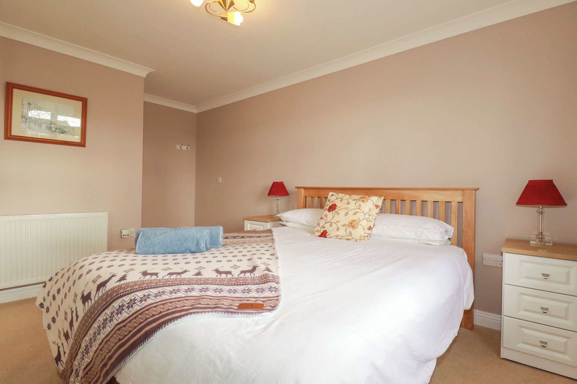 A bedroom with a bed, bedside tables, a lamp, a radiator, and a framed picture on the wall.