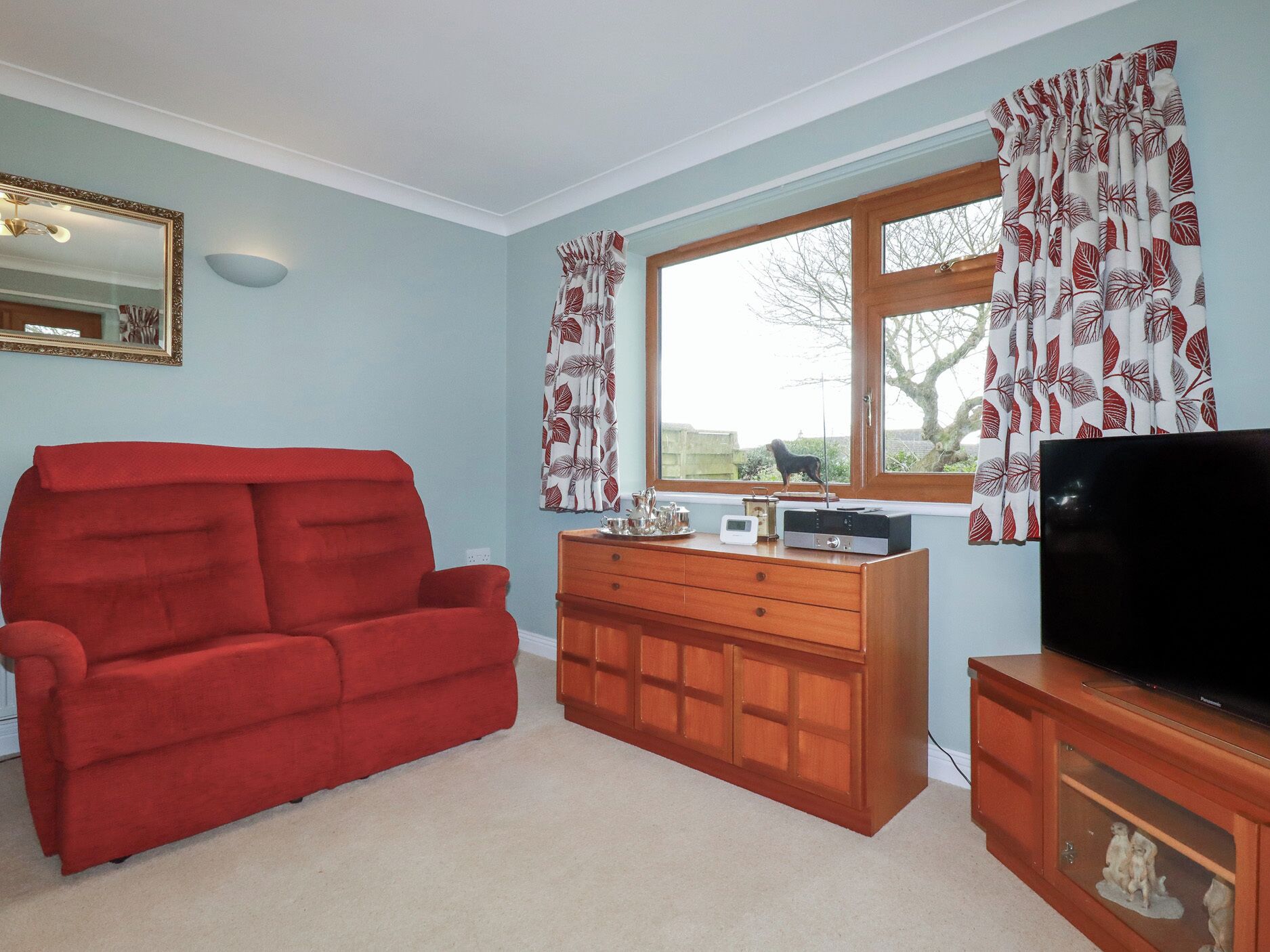 A living room with a red sofa, wooden cabinet, and a television.