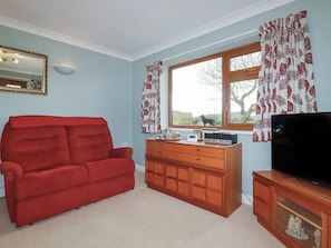 A living room with a red sofa, wooden cabinet, and a television. - Honeysuckle Rise (Looe)