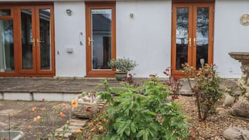 A white building with three wooden-framed glass doors, a small garden with various plants, and a stone sculpture.