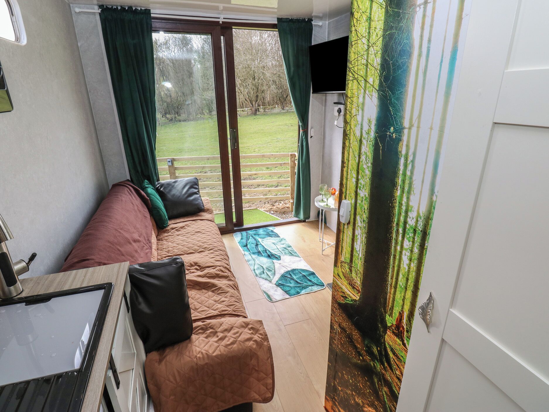 A cozy room with a bed, a small table with a glass, and a view of a grassy area through a sliding door.