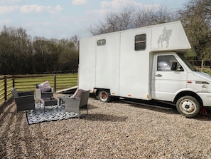 Una camper furgoneta IVECO blanca estacionada sobre grava, con un pequeño espacio de estar al aire libre.