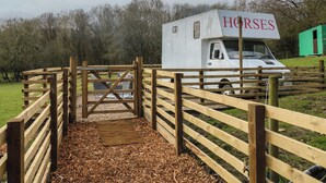 A white horse trailer with 'HORSES' written on it, parked in a fenced area with a wooden gate. - The Horse Box (Blaydon on Tyne)
