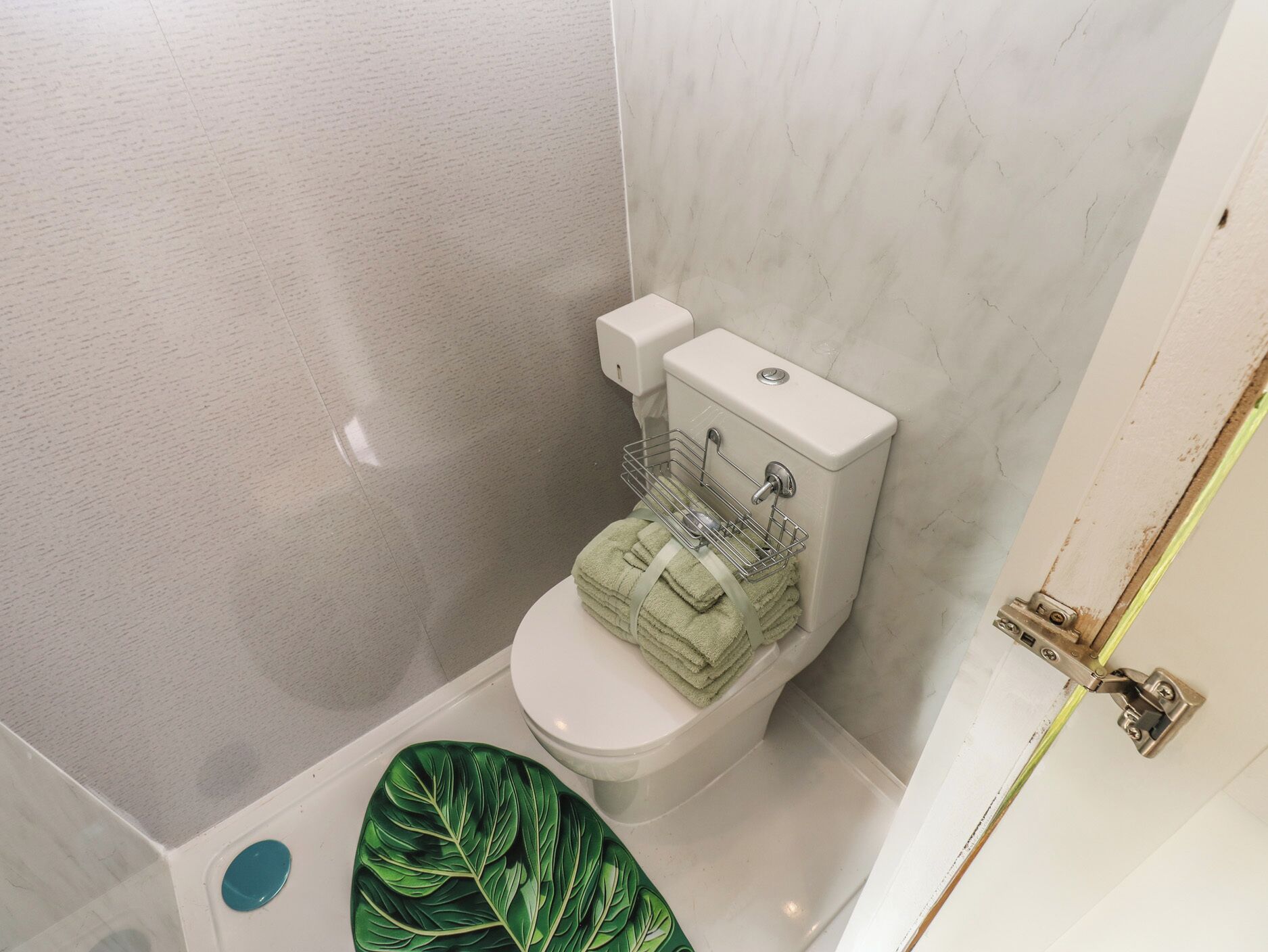 A bathroom with a toilet, a sink, and a green leaf-patterned mat.