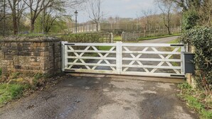 A gated entrance with a stone wall, a paved path, and a wooden fence in the background. - The Horse Box (Blaydon on Tyne)
