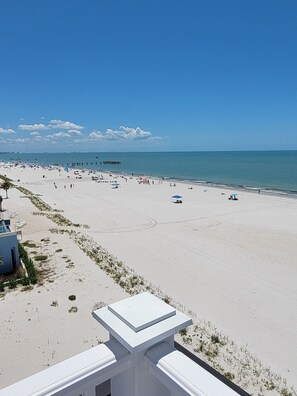 Ein Strand mit blauem Himmel, einem Pier in der Ferne und einigen Personen.