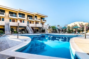 A swimming pool with a clear blue water, a building with balconies, and a clear sky. - The Orestis Cottage House , Stalos, Crete (Chania)