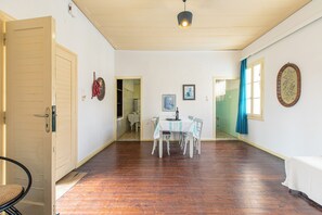 A spacious room with a wooden floor, a dining table with chairs, a bed, and a door leading to another room. - The Orestis Cottage House , Stalos, Crete (Chania)