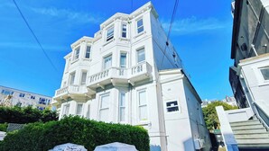 Un immeuble à plusieurs étages, doté d’une façade blanche, d’un balcon au deuxième étage et du numéro « 21 » sur le portail.