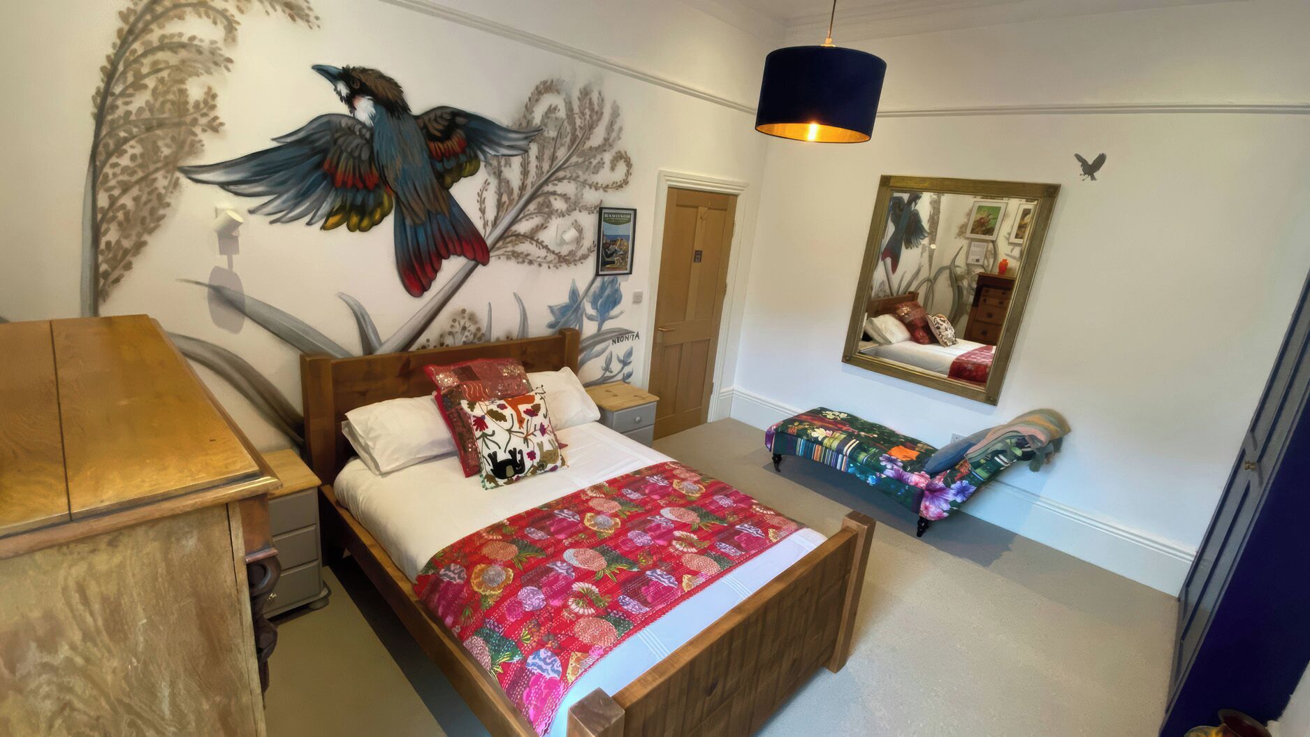 A bedroom with a wooden bed, a wooden nightstand, a bedside table, a mirror, and a wall mural.