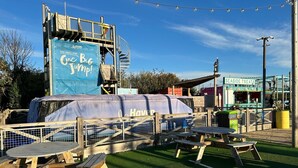 Een houten terras met picknicktafels, een overdekt gebied met een blauwe banner, en een bordje met de tekst 'Seaside Treats'.