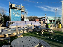 Una terraza de madera con mesas de picnic, un área cubierta con un banderín azul y un cartel que dice 'Seaside Treats'.