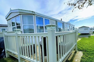 Una casa móvil con fachada blanca, un balcón y una terraza cercada.