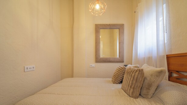 A bedroom with a bed, a bedside table, a mirror, and a hanging light fixture. - Casita de San Juan in Cartagena, Murcia, Spain. (Cartagena)