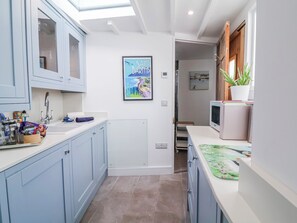 A kitchen with light blue cabinets, a white countertop, a framed picture of Saint Barthelemy, and a potted plant. - Hideaway Cottage (Bideford)