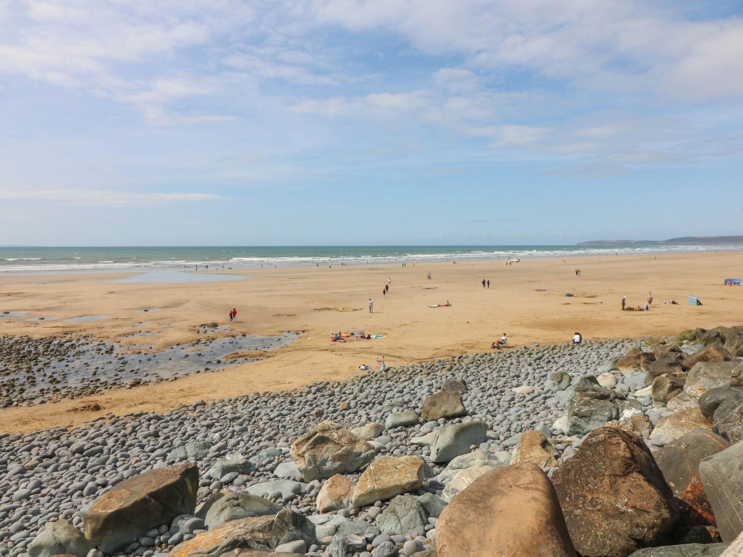 A beach with pebbles and rocks in the foreground, a sandy beach in the middle, and the ocean in the background.