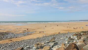 A beach with pebbles and rocks in the foreground, a sandy beach in the middle, and the ocean in the background.