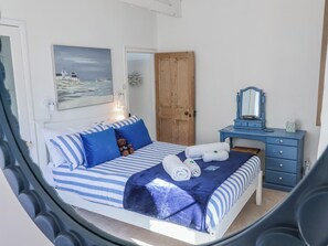 A bedroom with a bed, a wooden door, a dresser, a mirror, and a painting on the wall. - Hideaway Cottage (Bideford)