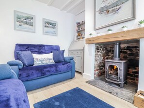 A living room with a blue sofa, a fireplace, and two framed paintings on the wall. - Hideaway Cottage (Bideford)