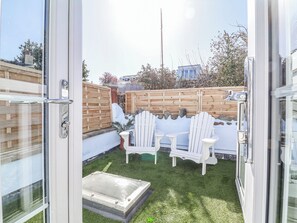 A patio area with a wooden fence, white chairs, and a small table. - Hideaway Cottage (Bideford)