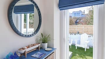 A room with a large mirror, a potted plant, a small table, and a view of a garden and outdoor seating area.