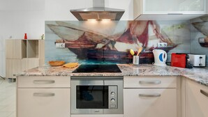 Eine moderne Küche mit Einbauofen, Dunstabzugshaube aus Edelstahl und einer Spritzschutzwand mit maritimen Motiven.