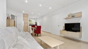 Ein modernes Wohnzimmer mit einer Couch, einem Couchtisch, einem an der Wand montierten Fernseher und einem Essbereich mit Stühlen und Tisch.