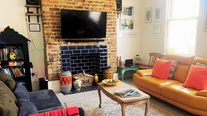 A living room with a brick fireplace, a sofa, a television, and a bookshelf. - 21 Gensing Road (St Leonards-On-Sea)