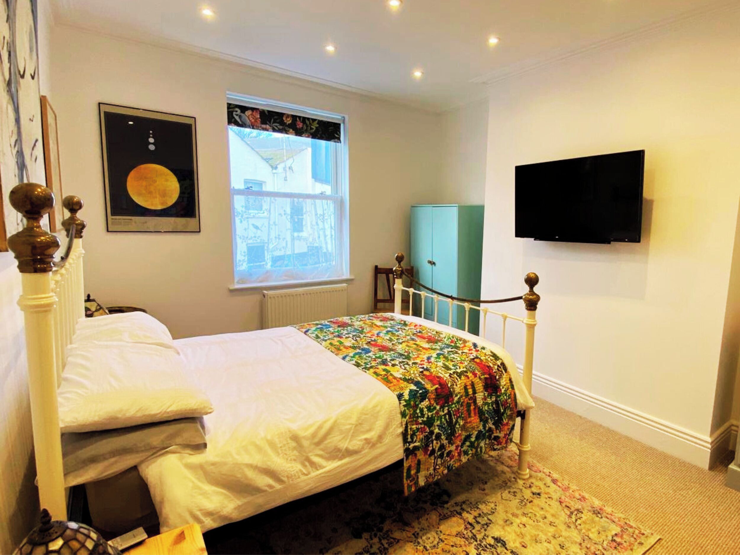 A bedroom with a bed, a window with a view, a television on the wall, and a cabinet.
