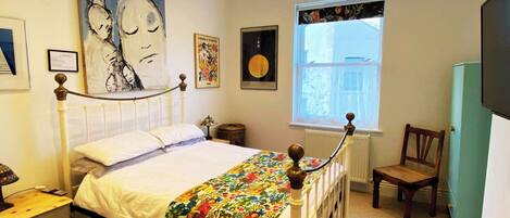 A bedroom with a bed, a chair, a window, and artwork on the walls.