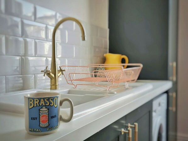 A kitchen with a white countertop, a brass faucet, a pink wire basket, and a mug with 'Brasso Metal Polish' text.