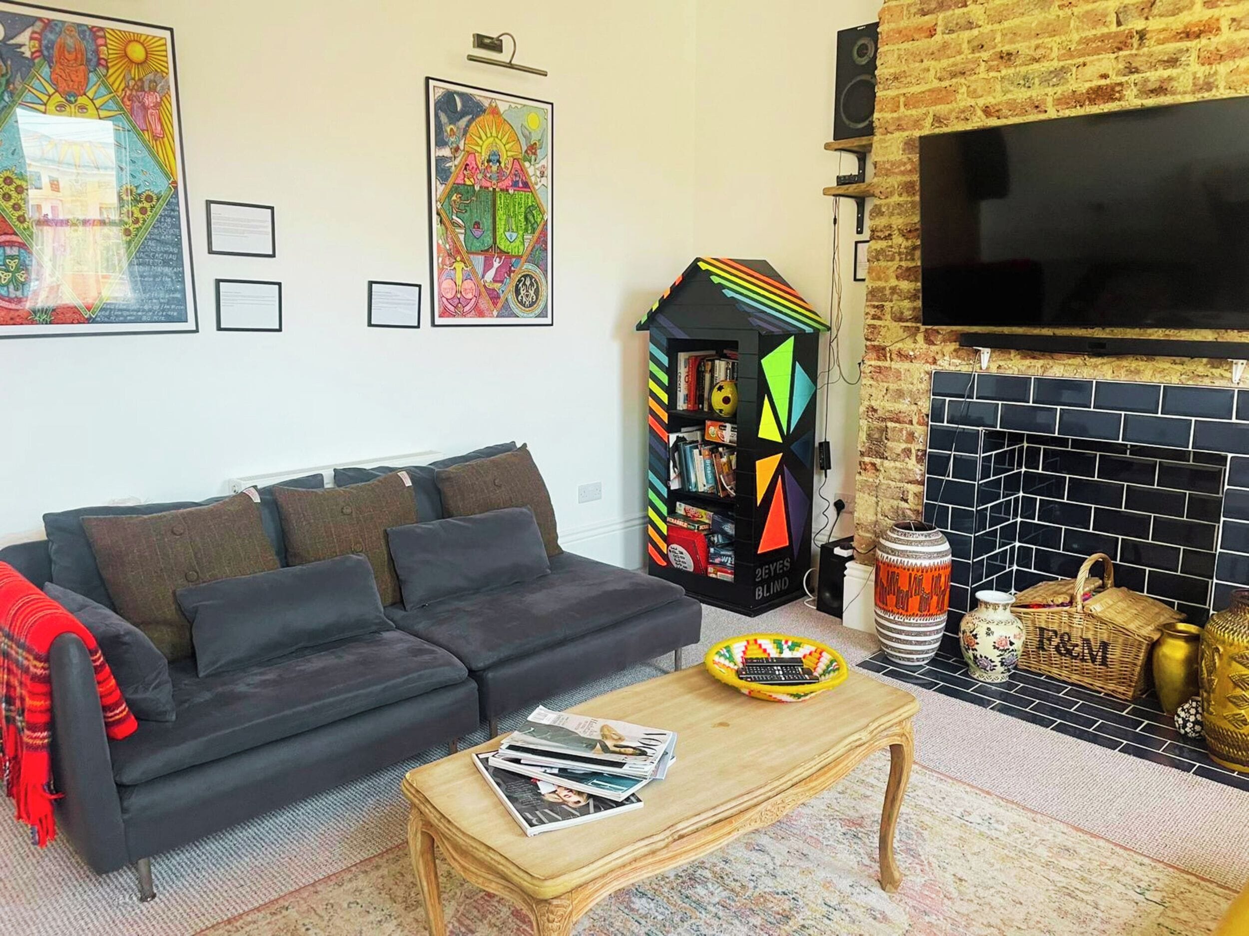 Una sala de estar con un sofá negro, una mesa de centro con revistas, una estantería colorida y una chimenea.