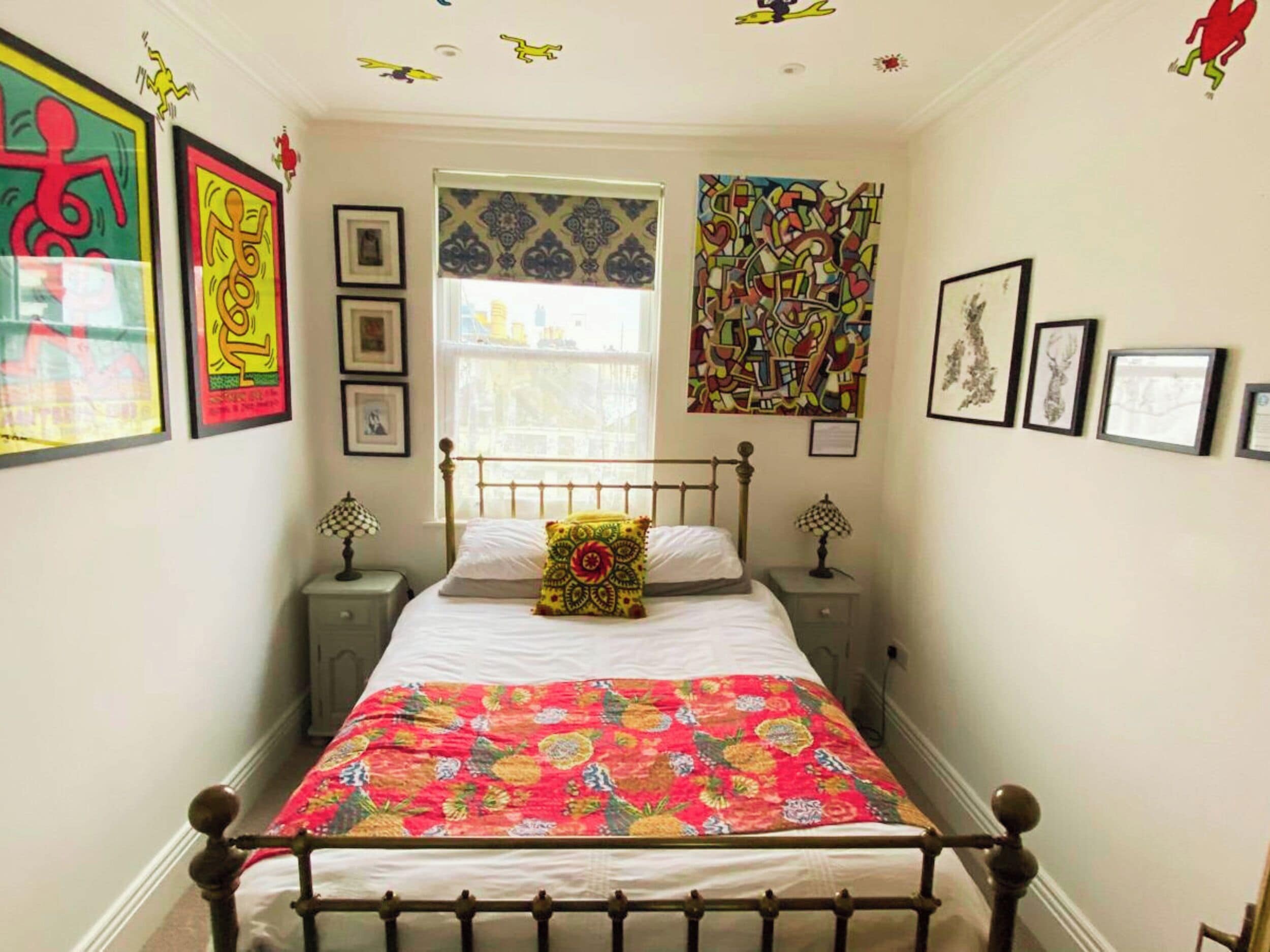 A bedroom with a bed, two bedside tables, a window, and various wall decorations.
