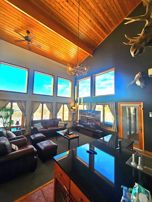 A living room with a large TV, leather sofas, a wooden ceiling, and a mounted deer head.