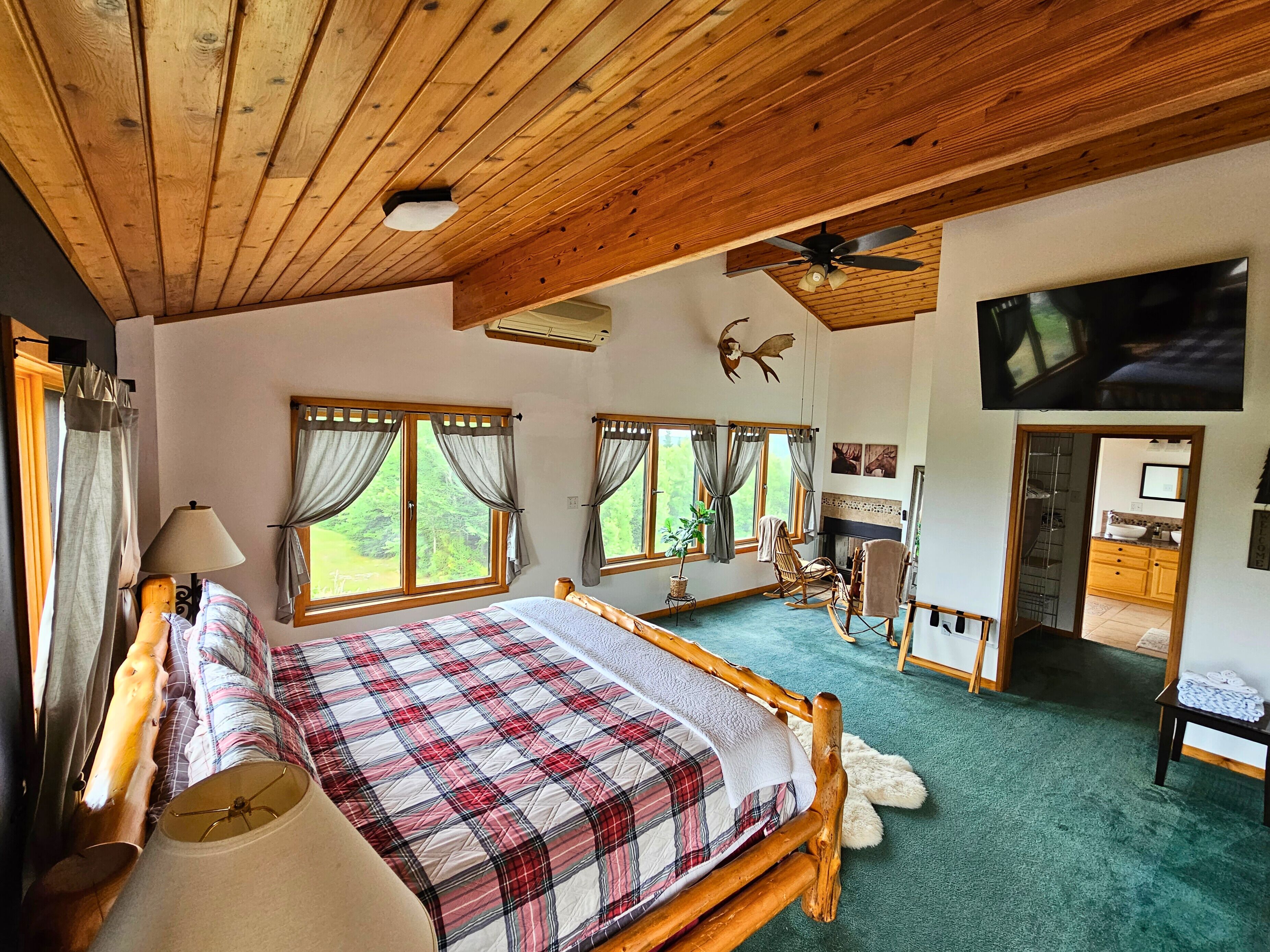 A spacious bedroom with a large bed, wooden ceiling, and multiple windows.