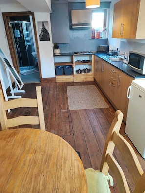 A compact kitchen with wooden cabinets, a microwave, and a sink. - The Courtyard Hideout (Hereford)