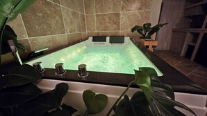 A hot tub with three jets, surrounded by large green plants, in a room with tiled walls. - LA SUITE TILLEUIL (Montgé-en-Goële)