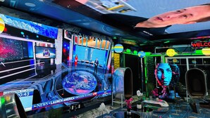 Uno schermo televisivo a tema spaziale, un cartello con la scritta 'WELCOME' e una sedia dal design futuristico.