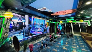 Un lounge futuristico con un grande schermo che mostra il conto alla rovescia per un lancio spaziale, zone relax e elementi decorativi.