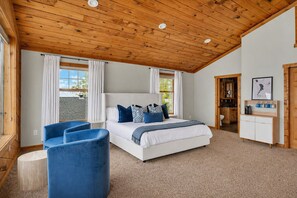 Ein Schlafzimmer mit einem Bett, einem blauen Sessel, einer Holzbalkendecke und Blick ins Freie.