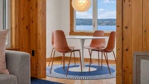 Een eetgedeelte met een tafel en stoelen, een uitzicht op een meer door een raam, en houten lambrisering.