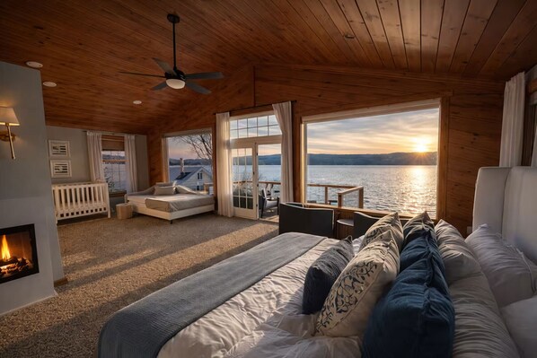 Ein gemütliches Cabin-Schlafzimmer mit Bett, Kamin, Deckenventilator und großem Fenster mit Seeblick.